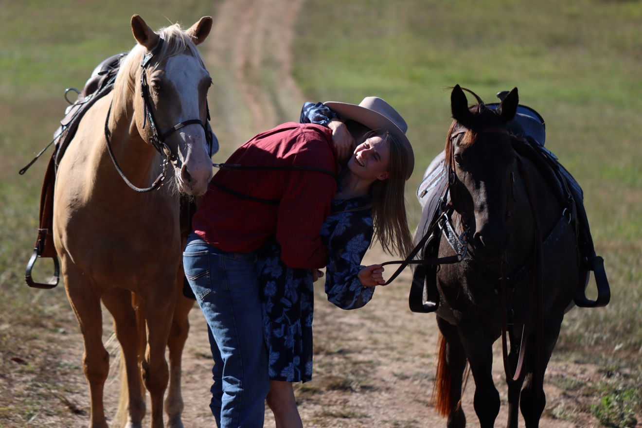 Luke and Kristi embracing and laughing in the pasture between their two horses right after she said yes